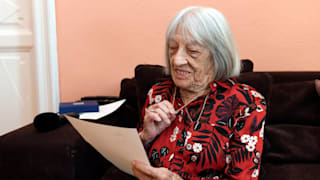 Agnes Keleti reading the letter sent by IOC President Thomas Bach, while holding the five-ring necklace received from the IOC
