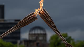 The atomic bomb dome stands in the background as Tokyo 2020 Olympic torch bearers exchange the flame during the torch relay in the Hiroshima Peace Park on May 17, 2021 in Hiroshima, Japan. Photo by Getty Images