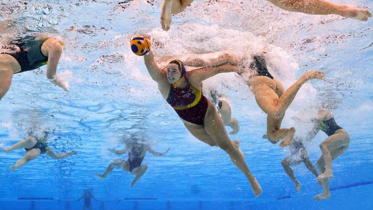 An underwater camera shot of nine female water polo players with the focus on one who is handling the ball.