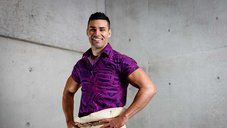 A male Tongan athlete in traditional dress poses during a photoshoot.