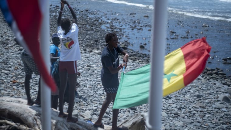 A group of athletes wave Senegalese flags on shore.