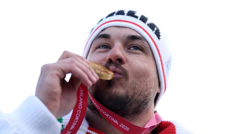 A close up of a male skier in Italian kit as he kisses his gold medal.