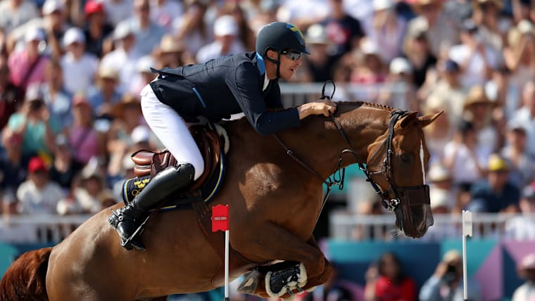 A male equestrian jumper makes a jump on a chestnut-coloured horse.