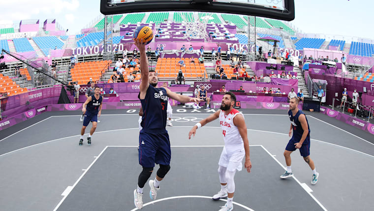 A male Serbian basketball player jumps for the basket on a 3x3 court.