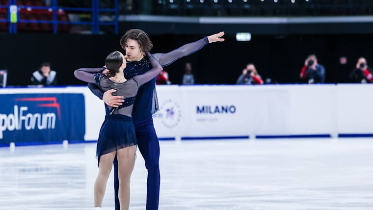 Pairs skaters in dark blue costumes strike a pose on the ice.