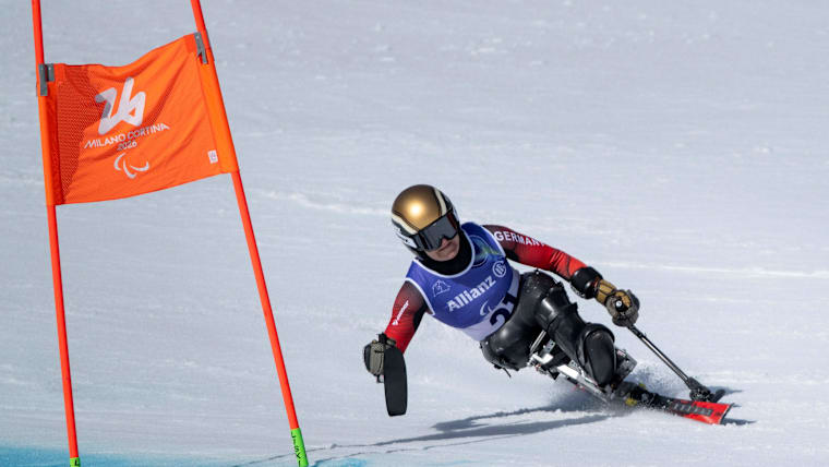 A female sit skier carves a turn around a gate on a downhill course.
