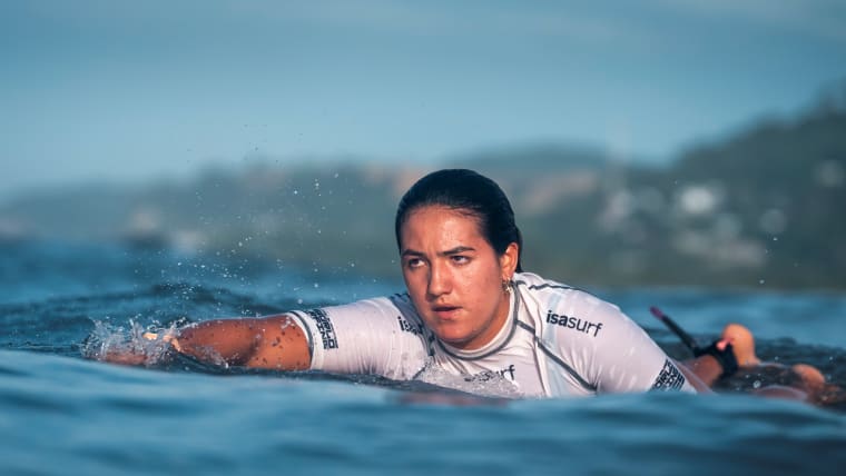 A female surfer paddles out in the ocean.