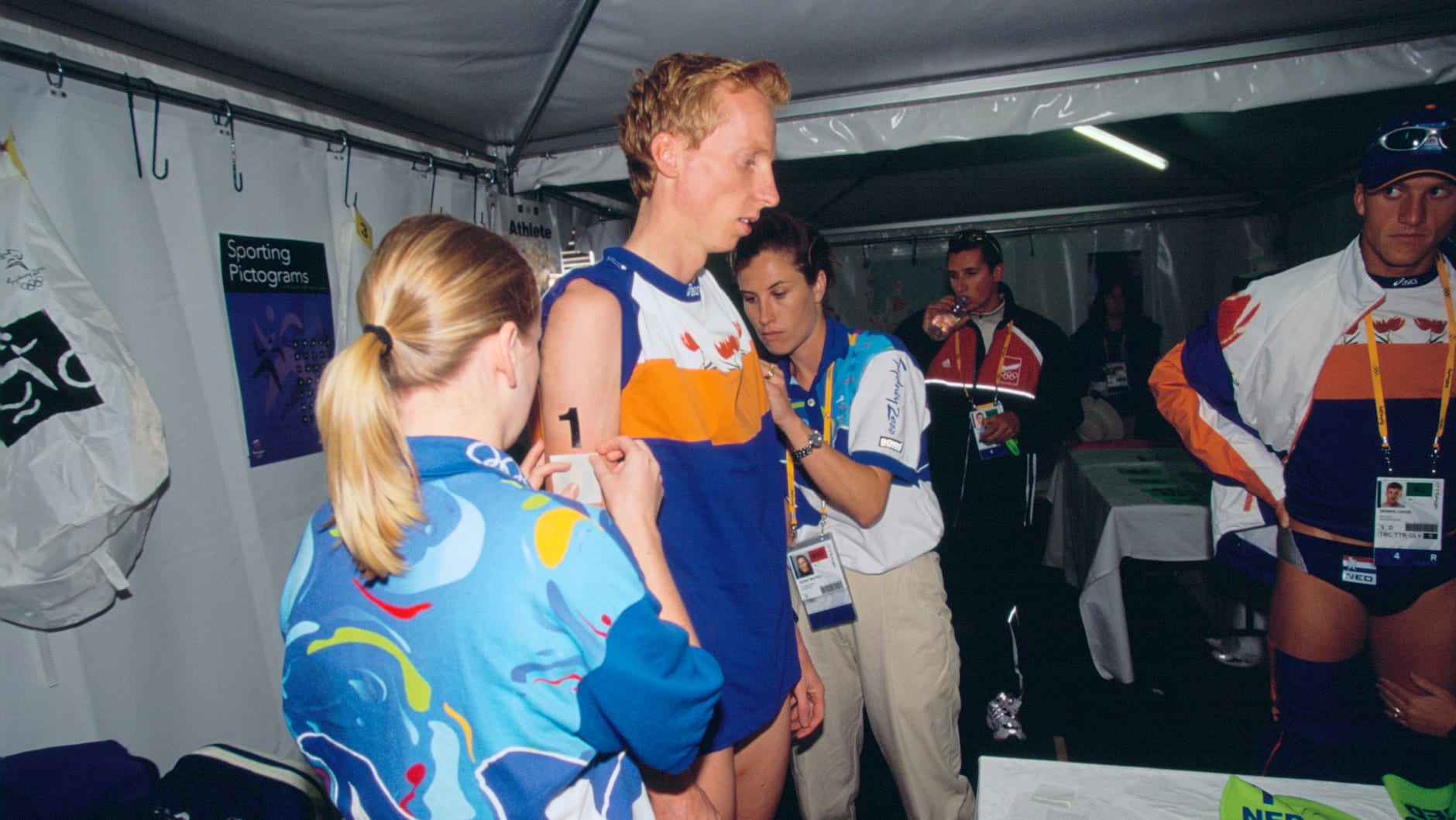 Volunteers assist a triathlete with tattooing (fake) number on their arm