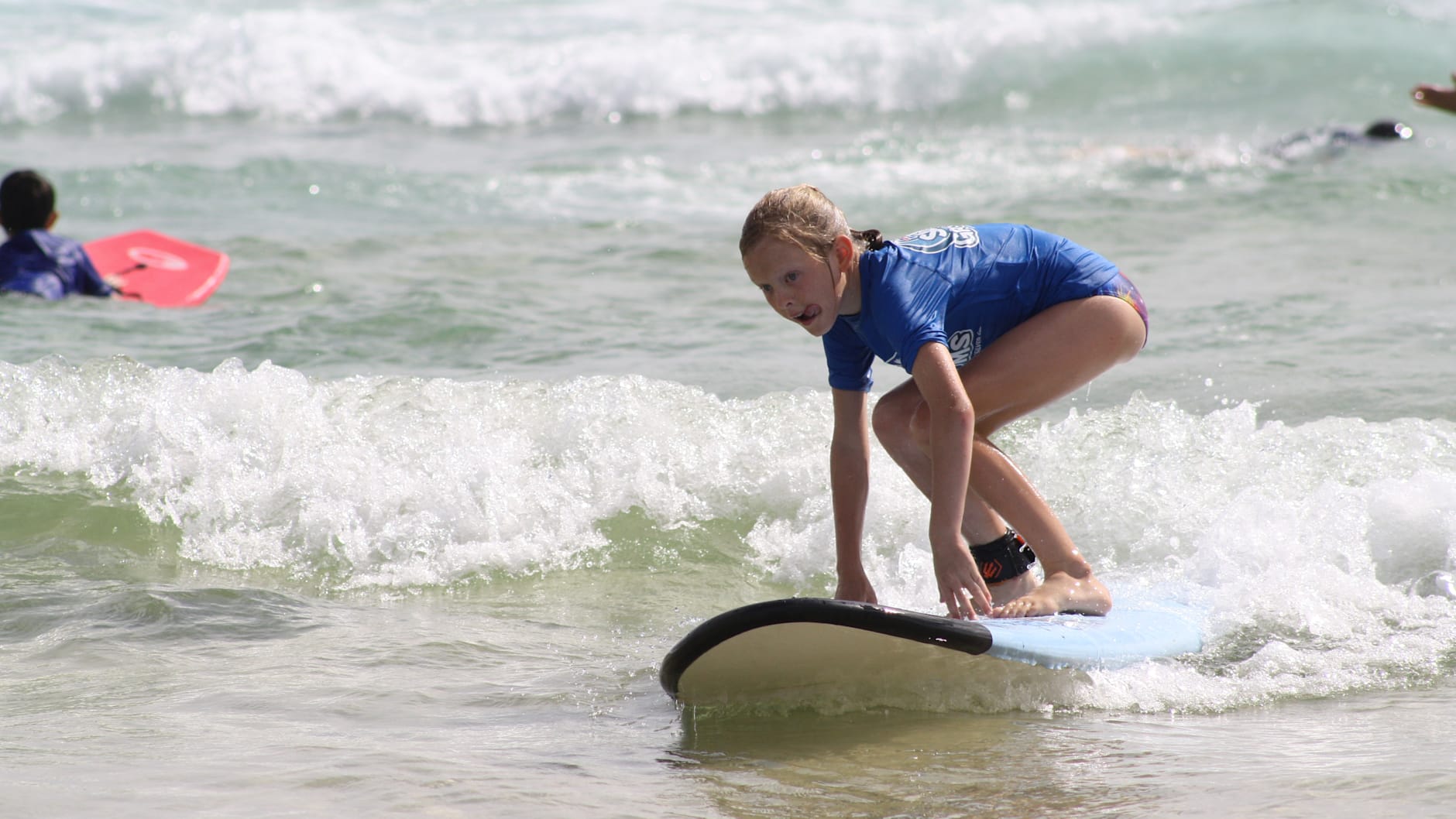 A young girl is balancing on a surfboard in the ocean.