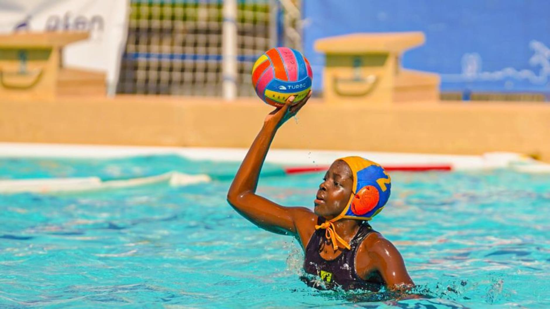 A young girl holds a water polo ball in her hand while in the water