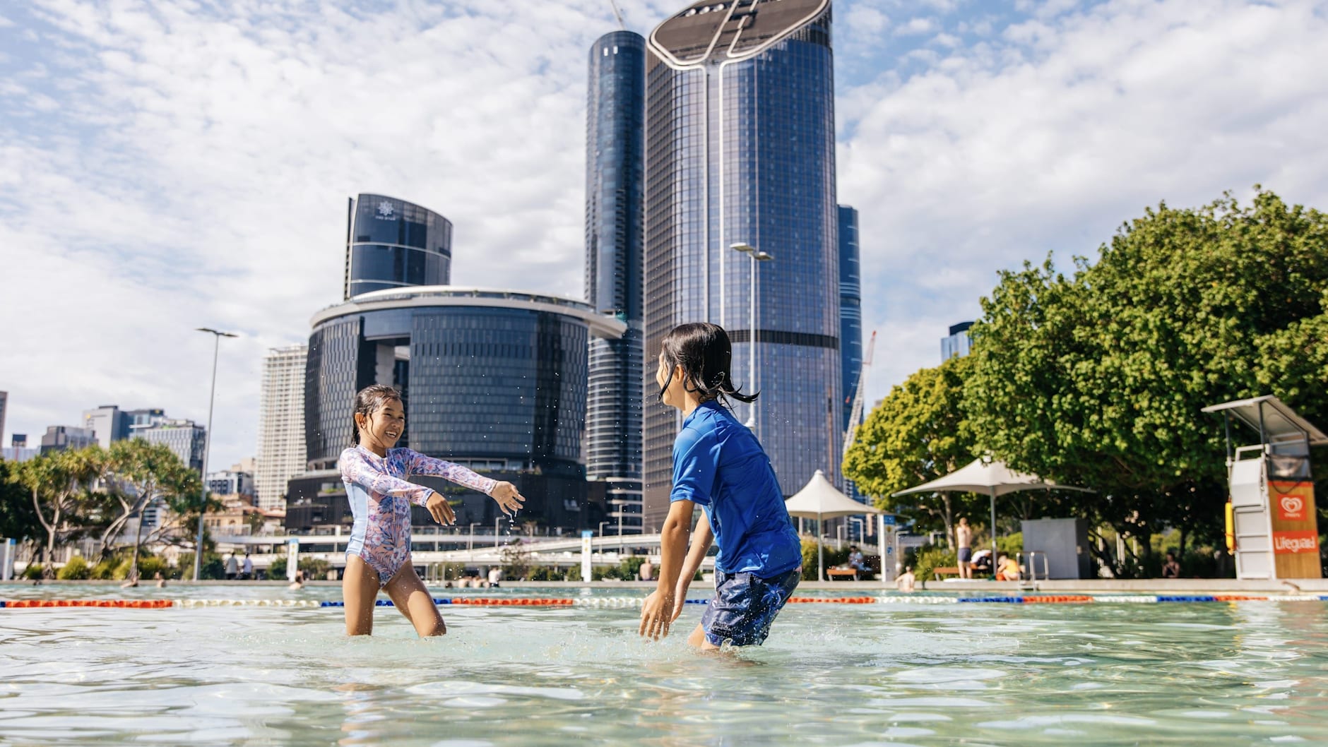 Two children splash each other at Streets Beach in Southbank. You can see The Star and 1 William street buildings in the background.