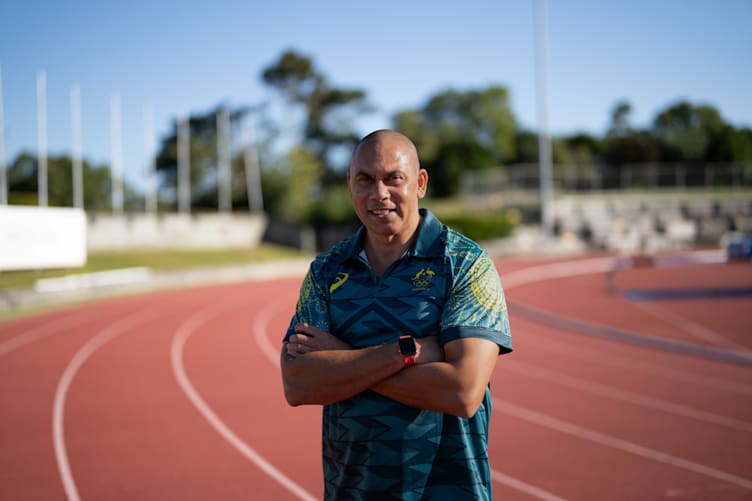 Patrick Johnson stands with his arms folded on his chest. Behind him is a running track.