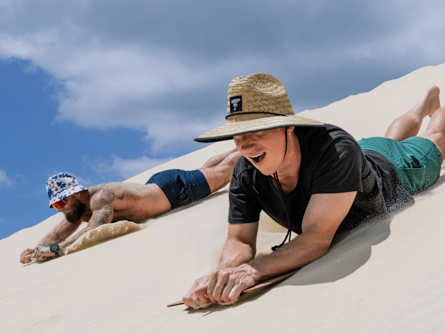 Two males sand tabogganing down the sand hills of Moreton Island.