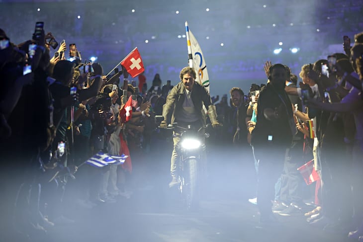 Tom Cruise membawa bendera Olimpiade keluar dari stadion