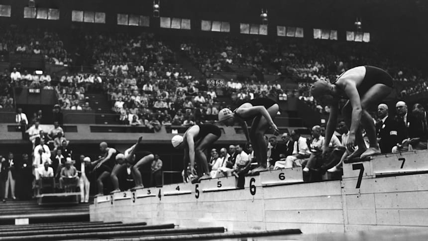 A black and white photo of female athletes lining up on the starting blocks before an Olympic swimming race in 1948