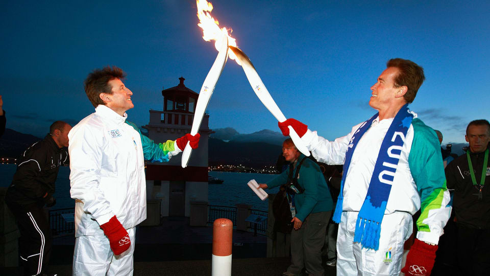 California Governor Arnold Schwarzenegger (R) hands the olympic flame to London 2012 chair Sebastian Coe of Great Britain ahead of the Vancouver 2010 Winter Olympics