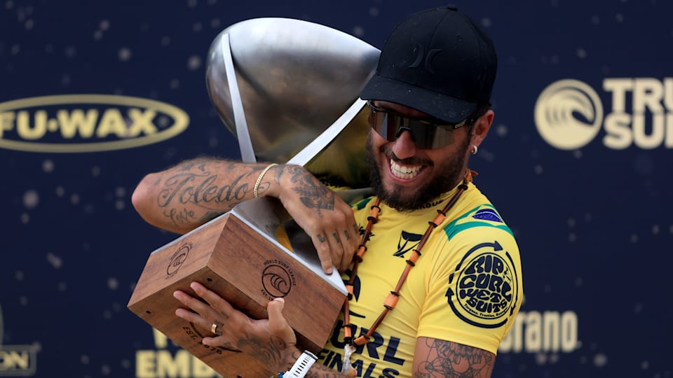 A male surfer clutches a trophy on stage after a competiiton.