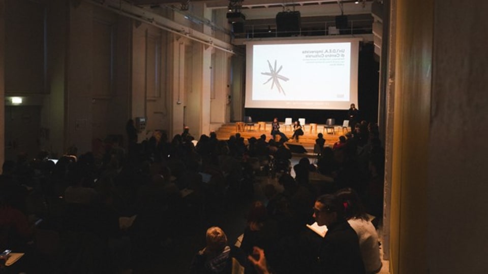 Foto della sala del BASE piena di persone mentre ascoltano il talk