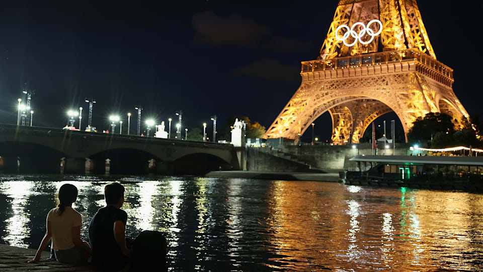 Spectators view the Eiffel Tower and Olympic rings along River Seine.