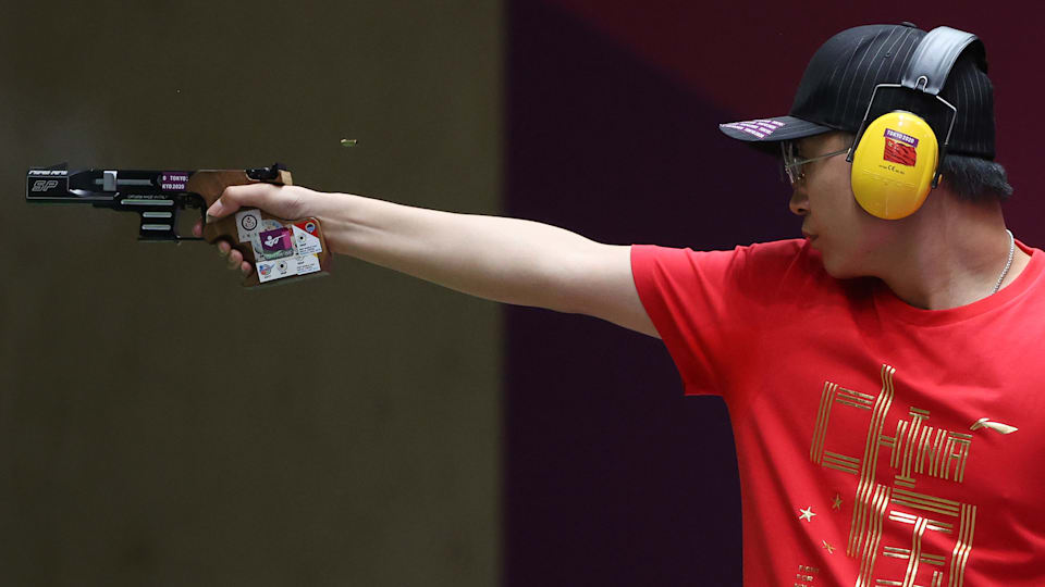 A male pistol shooter aims at a target.