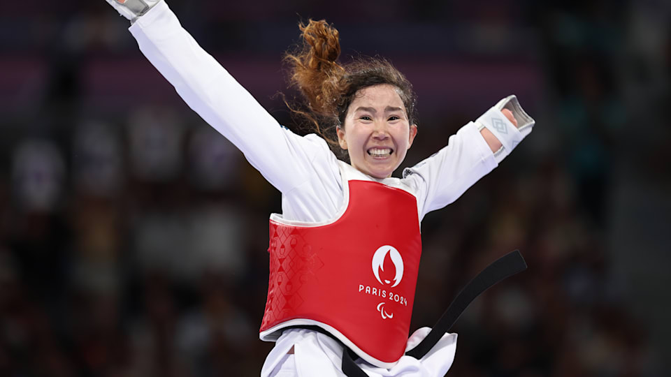 Zakia Khudadadi looks to the camera with arms raised in celebration after winning the Women's Taekwondo K44 -47kg Repechage contest before going on to claim a first ever medal for the Refugee Paralympic Team with bronze