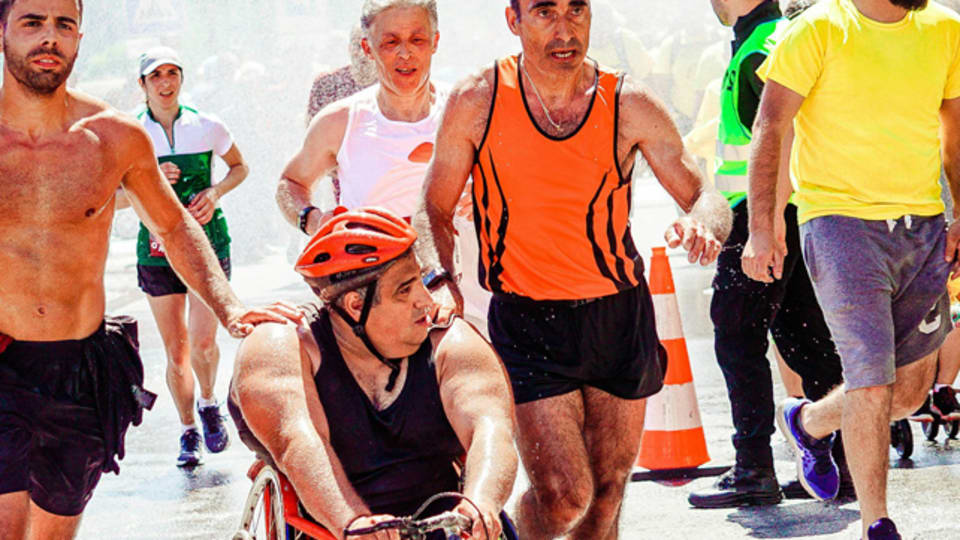 A gentleman in a wheelchair with a boy and a gentleman running alongside him