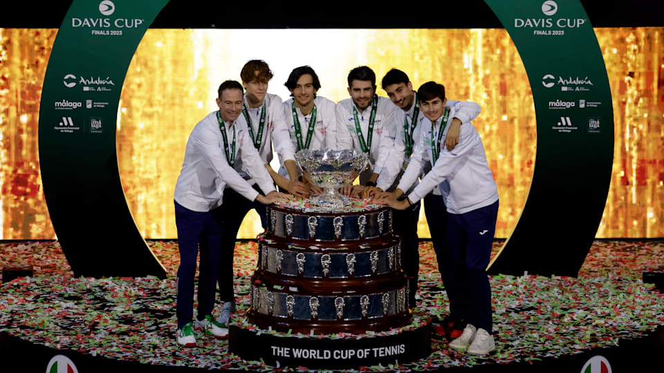 Italy's victorious Davis Cup team lean in around the trophy on a stage