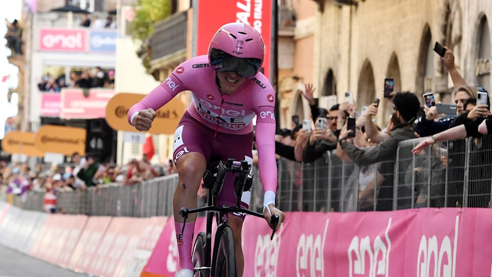 Pogacar, che indossa la maglia rosa e un casco aerodinamico rosa abbinato, tira un pugno in aria dopo aver tagliato il traguardo.
