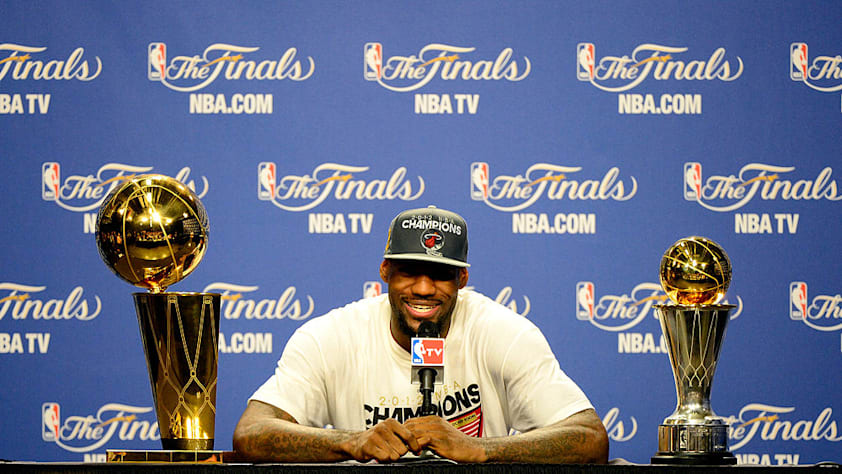  LeBron James #6 of the Miami Heat answers questions from the media next to the Larry O'Brien Finals Championship trophy and James' Bill Russell Finals MVP trophy.