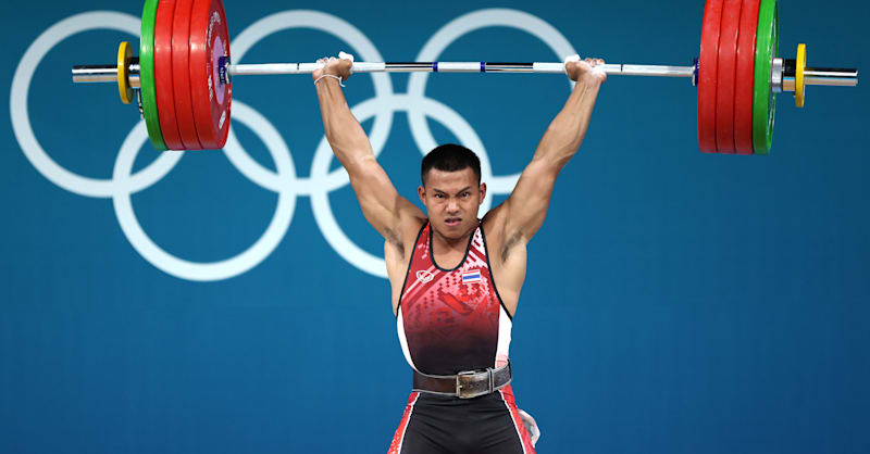 тяжелоатлет поднимает штангу над головой на соревнованиях